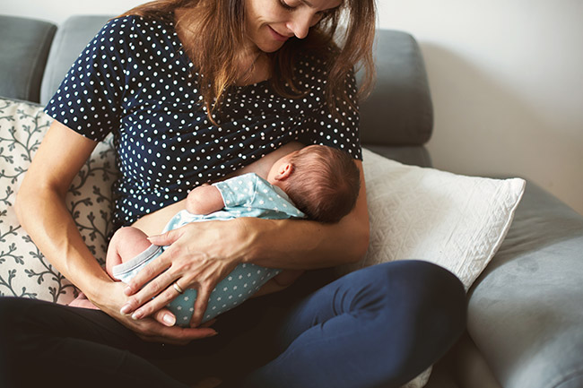 “Mother breastfeeding her newborn baby while seated on a couch.”